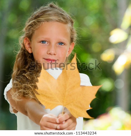 Close up portrait of blue eyed girl holding dry leaf in garden.