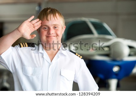 Portrait of young pilot with down syndrome saluting in hangar.