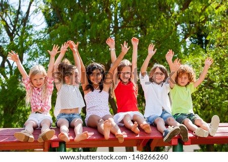 Group of children raising hands together in park.