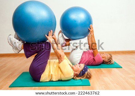 Two Senior women exercising muscles with Swiss balls in health club.
