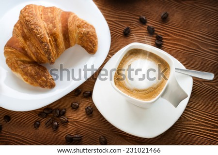 Top view of appetizing cappuccino with croissant on wooden table.