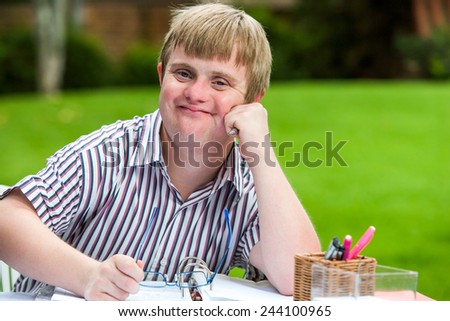 Close up portrait of young males student with down syndrome at desk holding glasses.