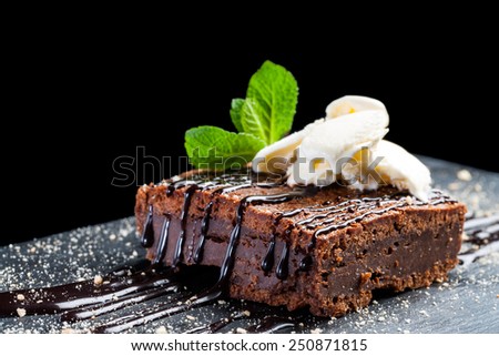 Macro close up of appetizing chocolate brownie with dark chocolate dressing and vanilla ice cream against black background.