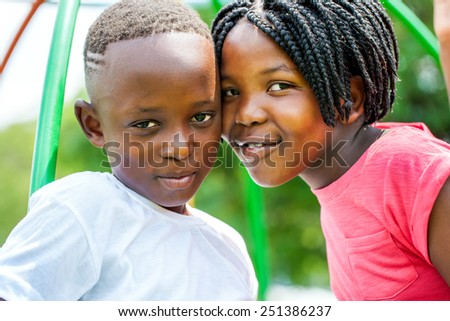 Close up portrait of little African brother and sister joining heads outdoors in park.