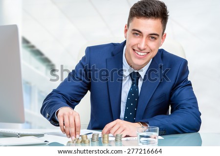 Close up portrait of young accountant counting money at desk. Young businessman in blue suit sitting at desk in office.