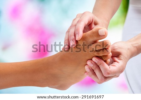 Extreme close up of physiotherapist doing reflexology massage on female foot. Colorful background.