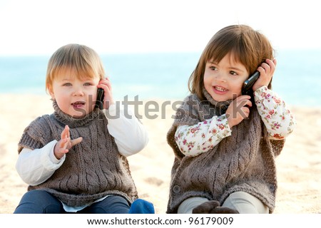 Portrait of two cute little girls on beach having conversation on mobile phones.