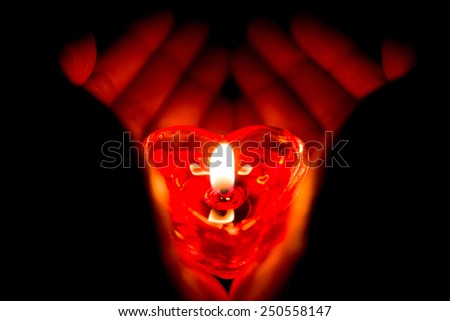 hands holding a heart shape burning candle in dark