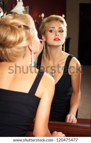 Elegant fashionable woman with diamond jewelry looks at herself in mirror. Fashion shoot.