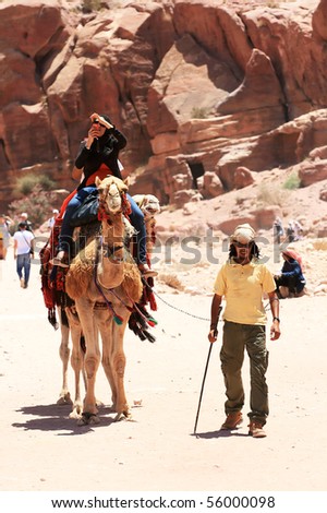 PETRA, JORDAN - JUNE 18: A tourist rides a camel and taking photos in beautiful Valley June 18 in Petra, Jordan. Cameleer walking next to the camel.