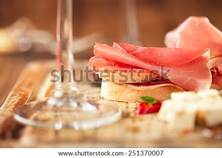 Cured Meat and ciabatta bread on wooden board, white wine on background