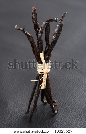 Vanilla pods  bunch tied by raffia on black leather background, shallow DOF, focus on the tops