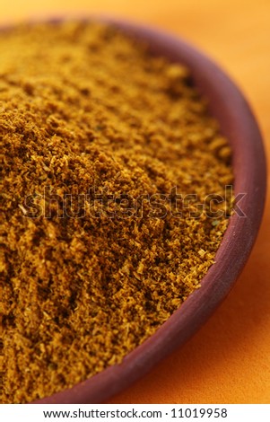pile of bright Madras Curry Powder in teraccotta dish on orange background, shallow DOF