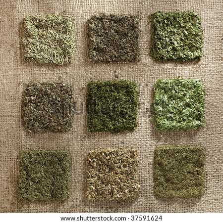 nine dried herb piles on jute hessian backdrop - rosemary, thyme, coriander leaves, basil, parsley, tarragon, dill, oregano, mint