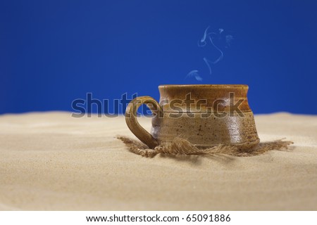 clay mug with tea or coffee on beach sand, blue background