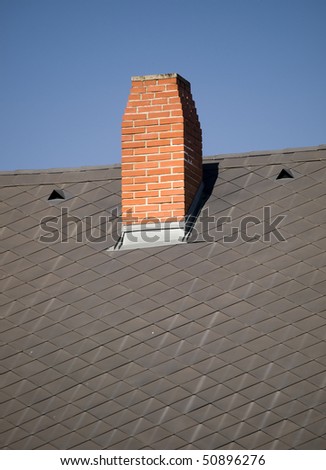 Terracotta bricks chimney on the dark grey metal-sheet roof