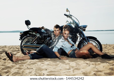 Young couple riders sitting together on sand beach by motorbike - travel concept