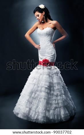 Beautiful bride brunette fashion model in bridal white dress with red ribbon and bow