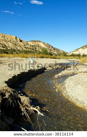 A small person hikes in the distance along a desert wash.