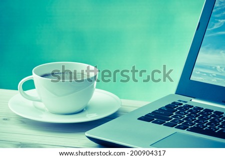 coffee cup with computer notebook on wood table with space for text in vintage color tone
