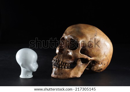 still life photography, old human skull with white ceramic child head on dark grunge background in confront concept