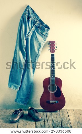 still life photography : old guitar with jeans hang on the wall and old leather shoes on old wood in rustic concept ( cross process color tone )