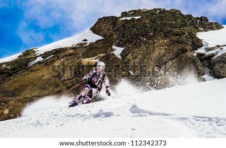 Woman skier in the deep snow. Against the background of the cliff. Raises the snow dust.