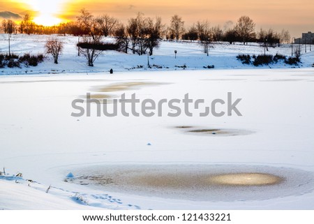 Man ice fishing alone on the pond at sunset