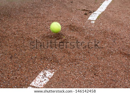Flying yellow ball and Old tennis court surface is red and ruined the line marking