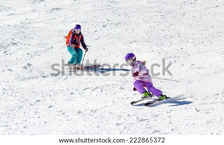 Little girl on skis in soft snow under the care of my mother on a sunny day in the mountains