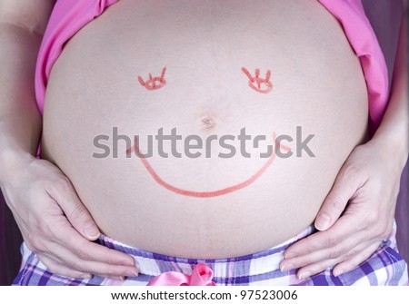 Painted red happy smiley face on the belly of pregnant woman