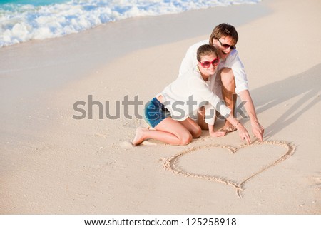 portrait of young happy couple drawing a heart on the sand