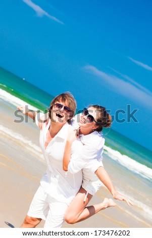 happy young couple in white clothes and sunglasses smiling on beach
