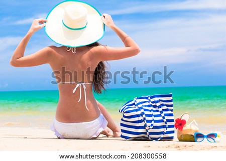 back view of a woman with stripy bag and straw hat at tropical beach