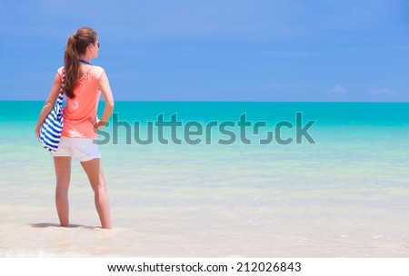 back view of a fit young woman with stripy bag at tropical beach