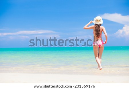 back view of a fit young woman in hat walking in the sea