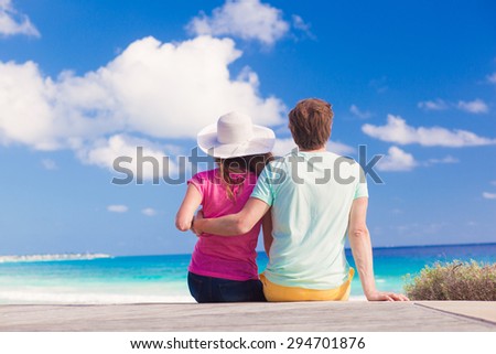 back view of happy young caucasian couple sitting at the beach