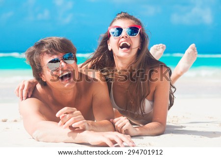 Closeup of happy young caucasian couple in sunglasses smiling at beach lying on sand