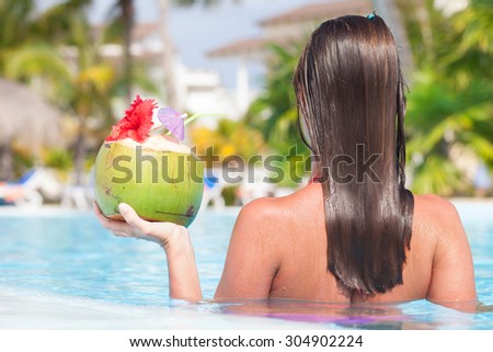 Beautiful long haired young woman in sunglasses with coconut cocktail in hand in luxury pool