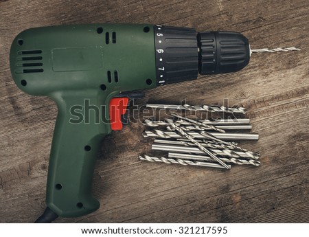 Drill and set of drill bits with screws on wooden background