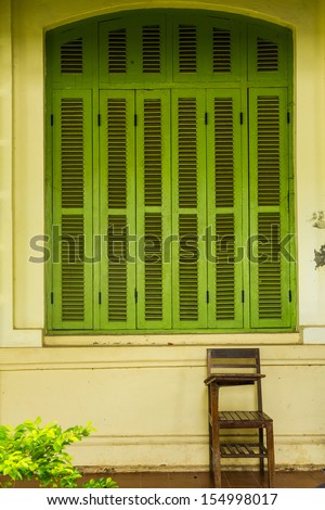 Green vintage wooden windows with student chair, colonial style building from Vientiane, Laos.