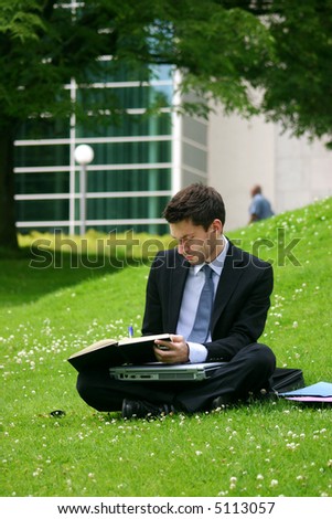 business man with laptop working in the park in front of office buildings