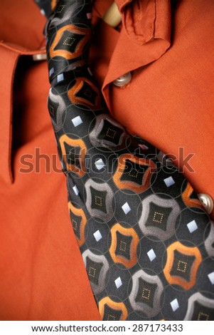 A close shot of a bright orange dress shirt with matching tie laid out. Shallow depth of focus with focus on tie in center of image.