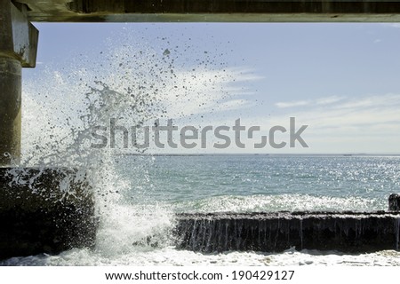 sea spray from a wave breaking under a concrete bridge on a hot day
