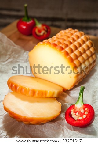 A round of cheese placed on packaging paper with red chili on a wooden cutting board in a dark corner