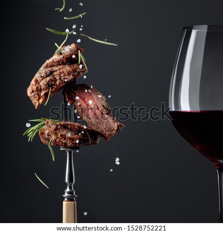 Grilled ribeye beef steak with rosemary and red wine on a black background. Beef steak on a fork sprinkled with rosemary and sea salt.   