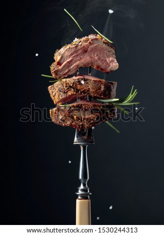 Grilled ribeye beef steak with rosemary on a black background. Beef steak on a fork sprinkled with rosemary and sea salt.   