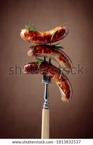 Grilled sausages with rosemary. Hot sausages on a fork sprinkled with rosemary.