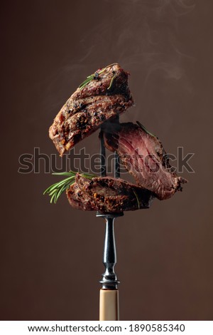 Grilled ribeye beef steak with rosemary on a brown background.  Beef steak on a fork.