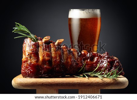 Glass of beer and grilled pork ribs with rosemary on a wooden board. Copy space.